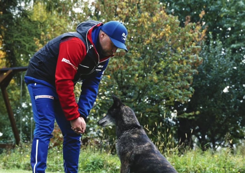 Adam se sklání k sedícímu belgickému ovčákovi na zahradě